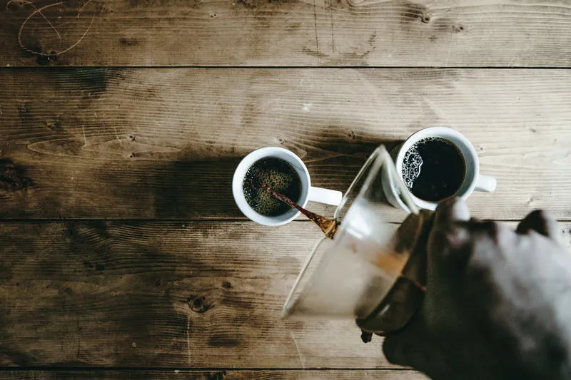 木のテーブルで、コーヒーを白いマグカップに注ぐところ